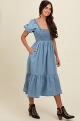 woman wearing a light blue smocked waist midi dress with puff sleeves and pockets, styling with black western boots