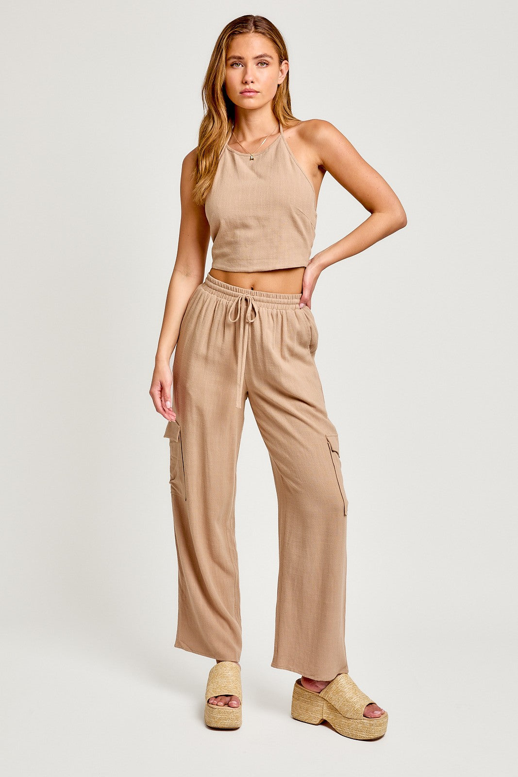 woman wearing a beige cropped tank top and matching wide-leg cargo pants with side pockets and platform sandals