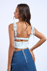 woman wearing a light blue floral crop top with ruffled straps and a back zipper, paired with a denim skirt