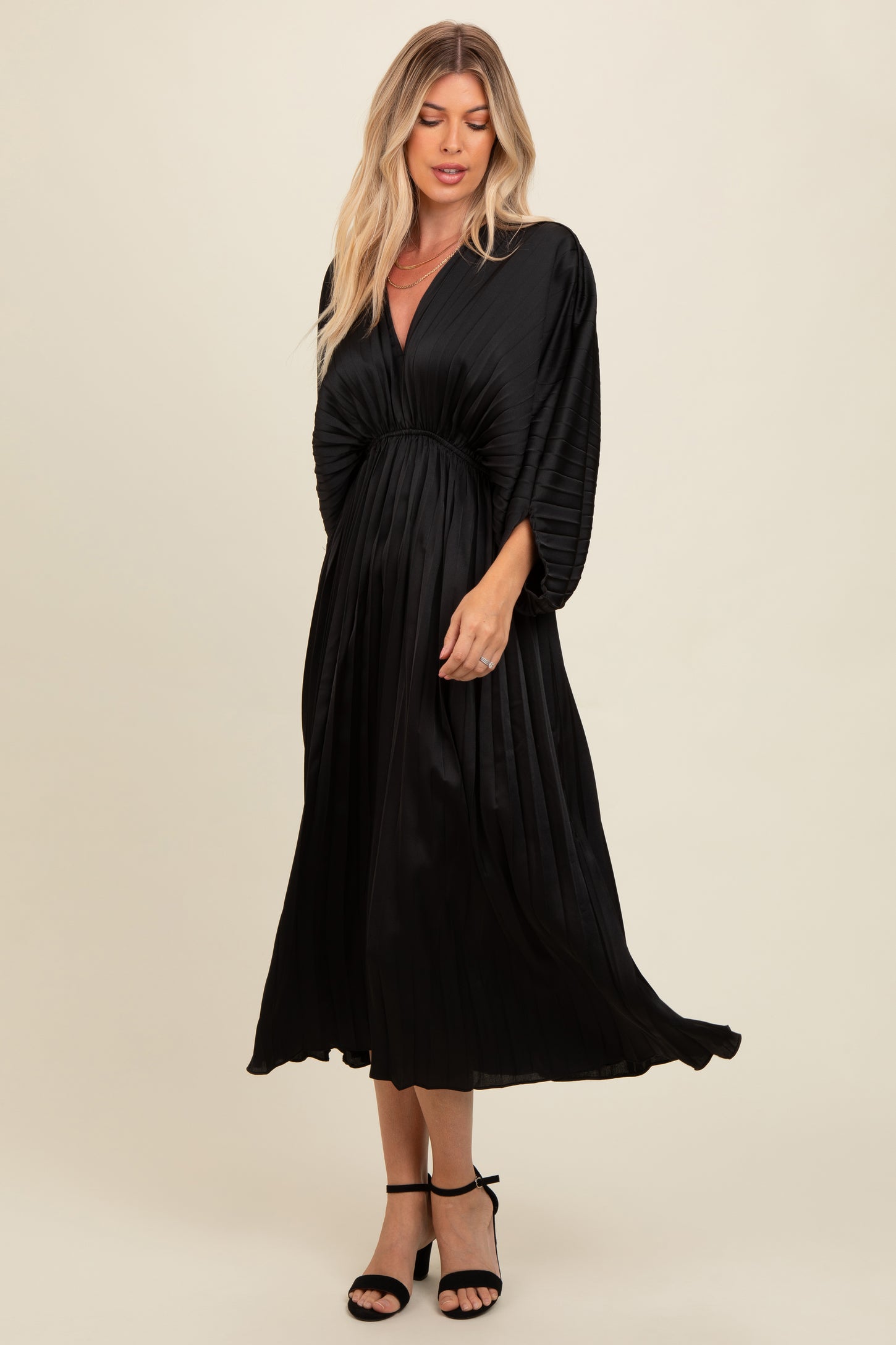 woman wearing a black pleated maxi dress with a deep v-neck and batwing sleeves, styled with strappy heels