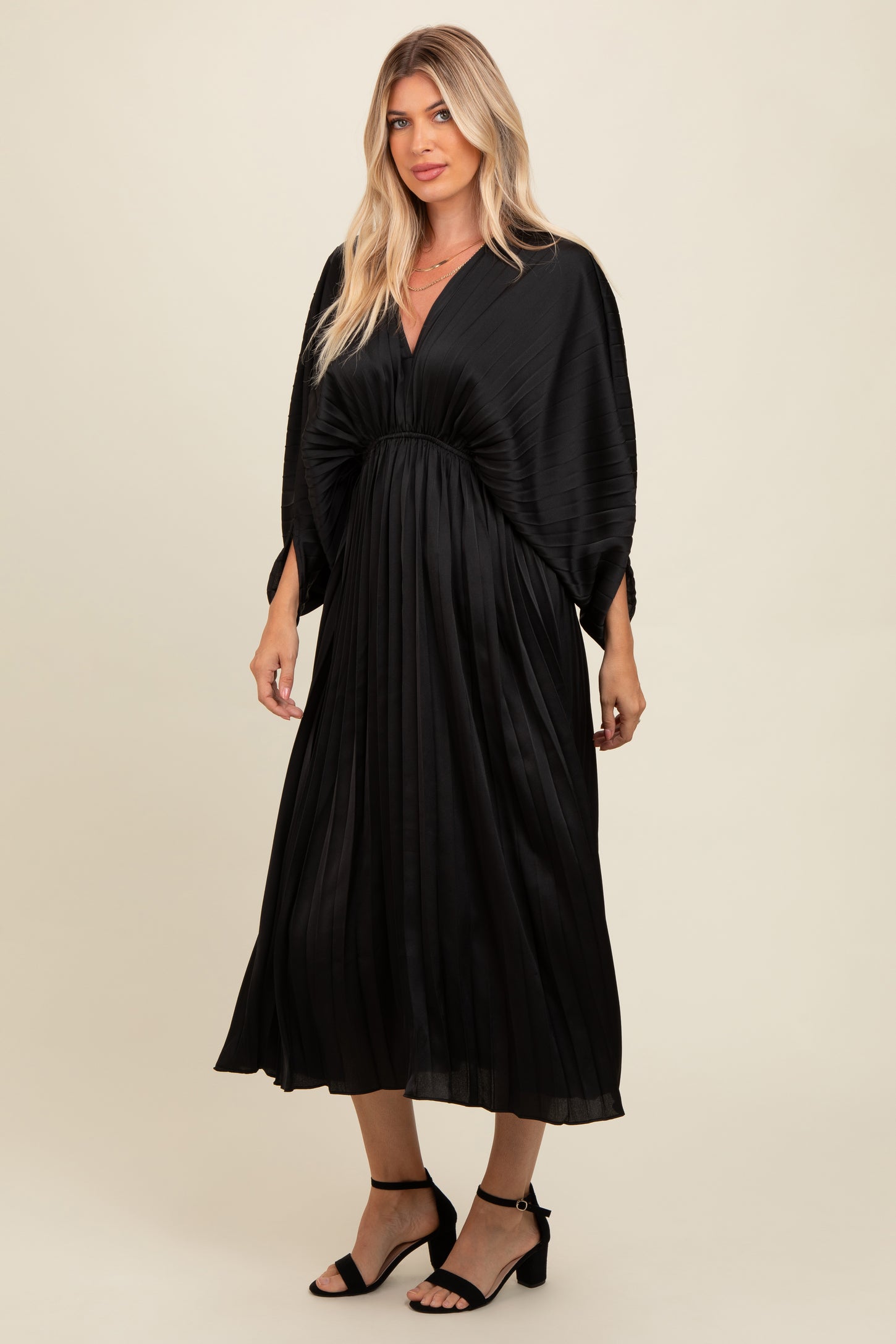 woman wearing a black pleated maxi dress with a deep v-neckline and oversized sleeves