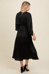 woman wearing a black pleated midi dress with three-quarter sleeves, showing the back view