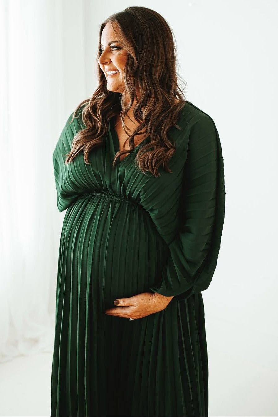 woman wearing a dark green pleated maternity dress and holding her baby bump