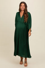 woman wearing a deep green pleated maternity dress with a v-neck and flowing sleeves, showcasing her baby bump