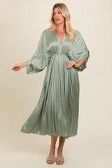 woman wearing a light green pleated maxi dress with a deep v-neck and wide sleeves