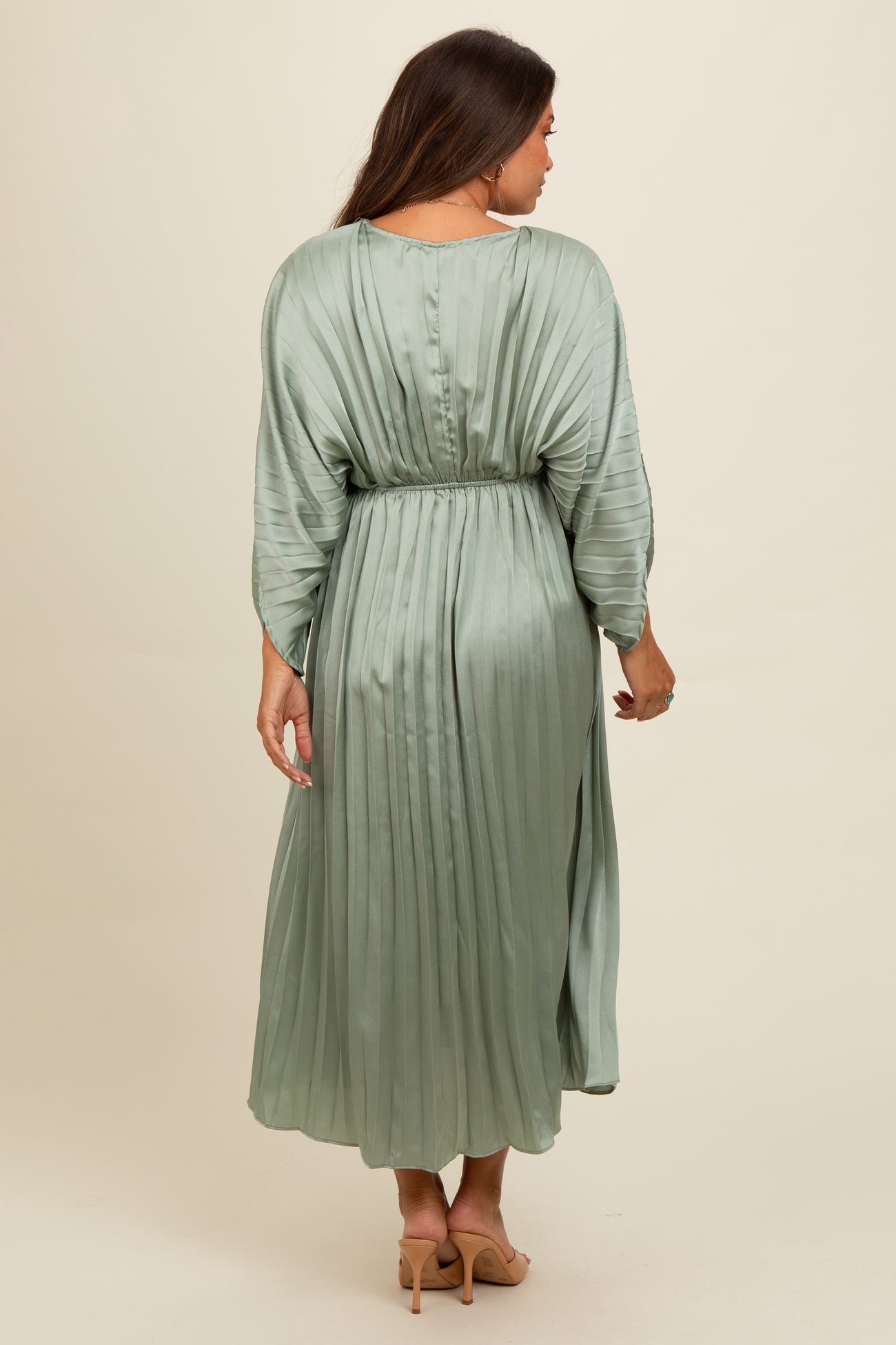woman wearing a pleated sage green maternity dress with three-quarter sleeves and a cinched waist