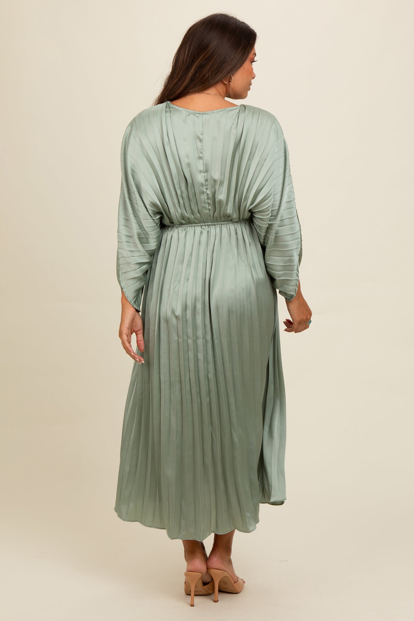 woman wearing a pleated sage green maternity dress with three-quarter sleeves and a cinched waist