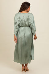 woman wearing a pleated sage green maternity dress with three-quarter sleeves and a cinched waist