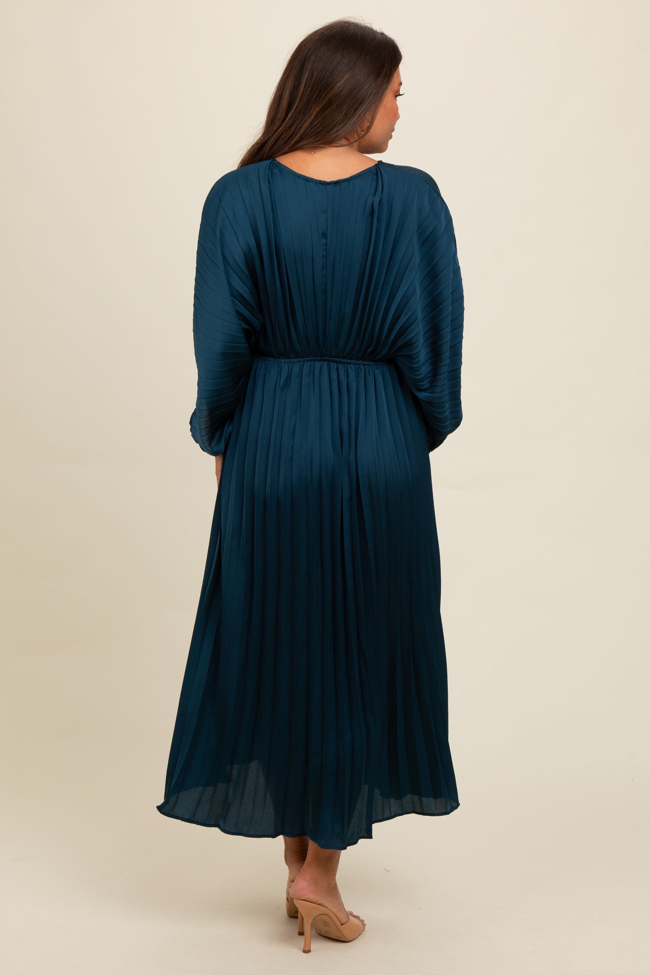 woman wearing a teal pleated maternity dress with three-quarter sleeves and cinched waist, showing a flowing silhouette