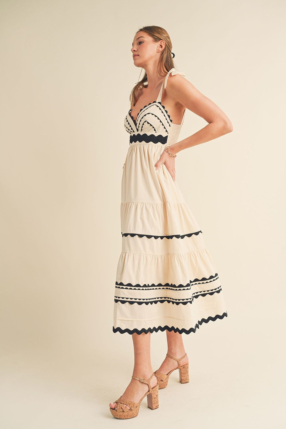 woman wearing a cream tiered dress with black scalloped details and straps, paired with tan platform heels