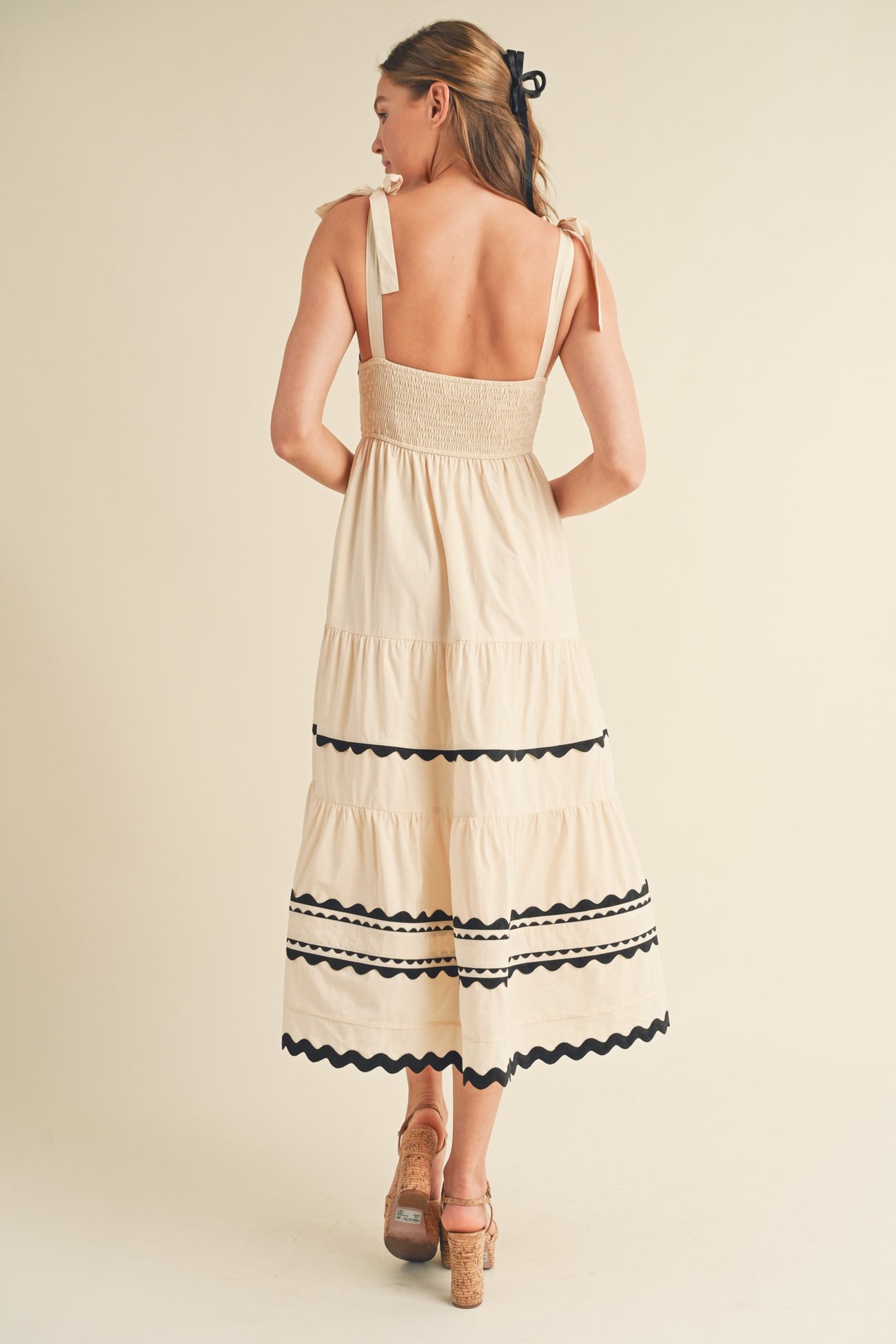 woman wearing a cream tiered midi dress with black trim and bow shoulder straps, shown from the back
