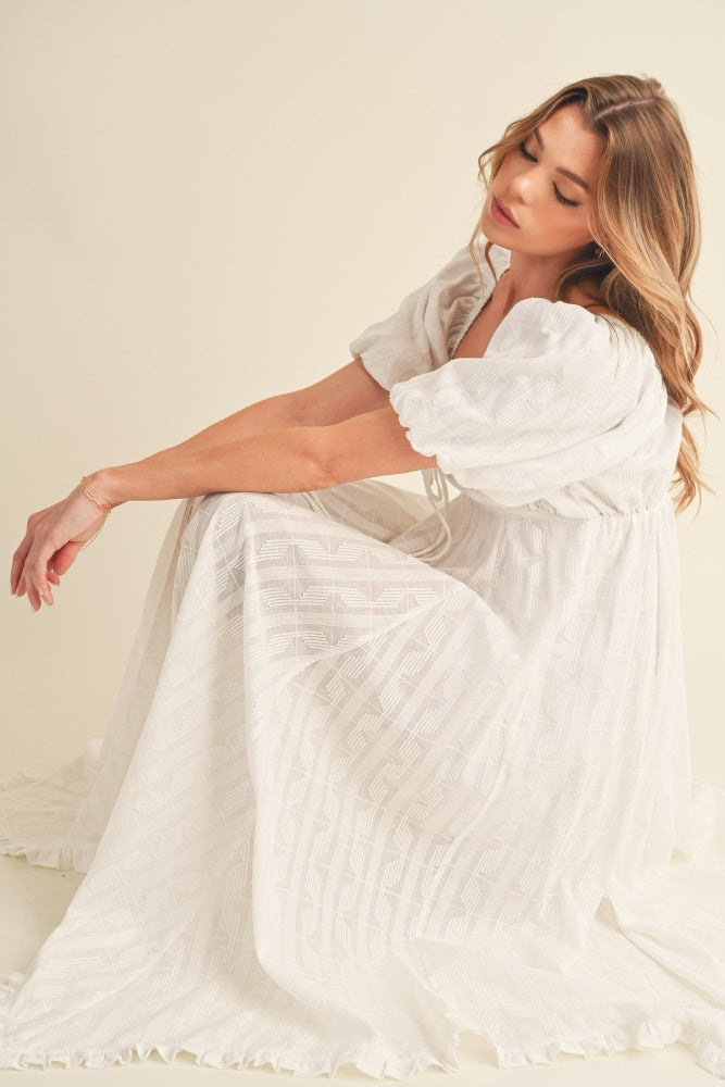 woman wearing a white puff sleeve maxi dress with a flowing skirt and textured fabric, sitting elegantly