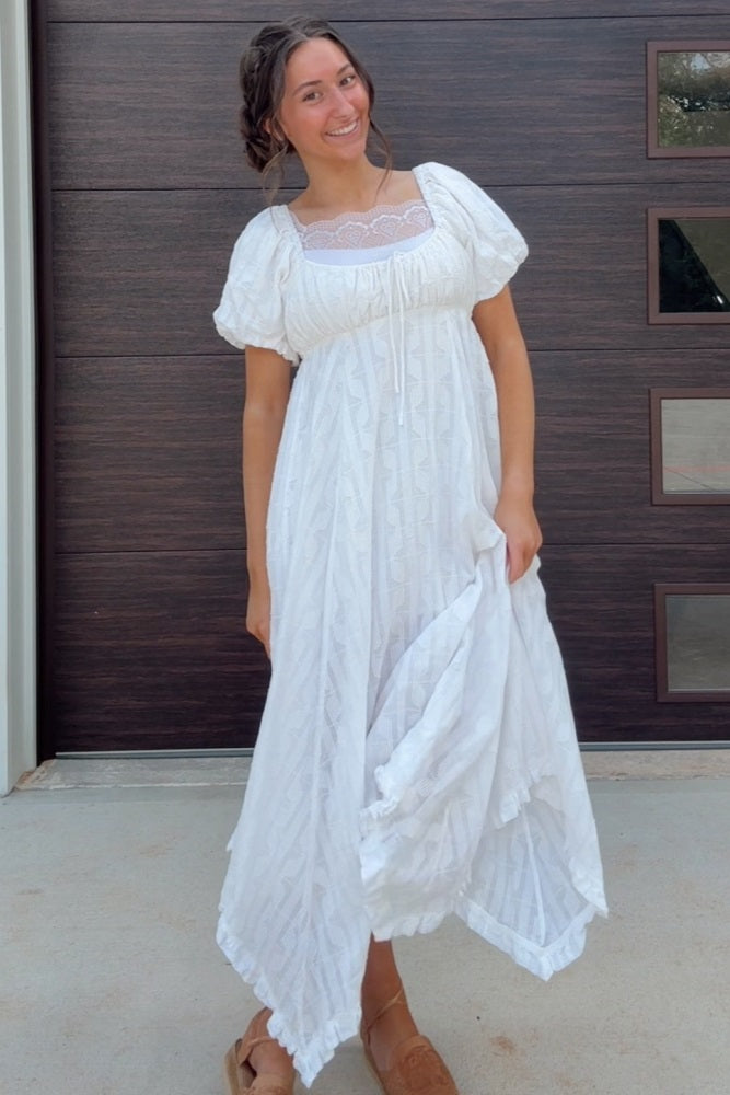 woman wearing a white maxi dress with puff sleeves and intricate detailing, standing outdoors