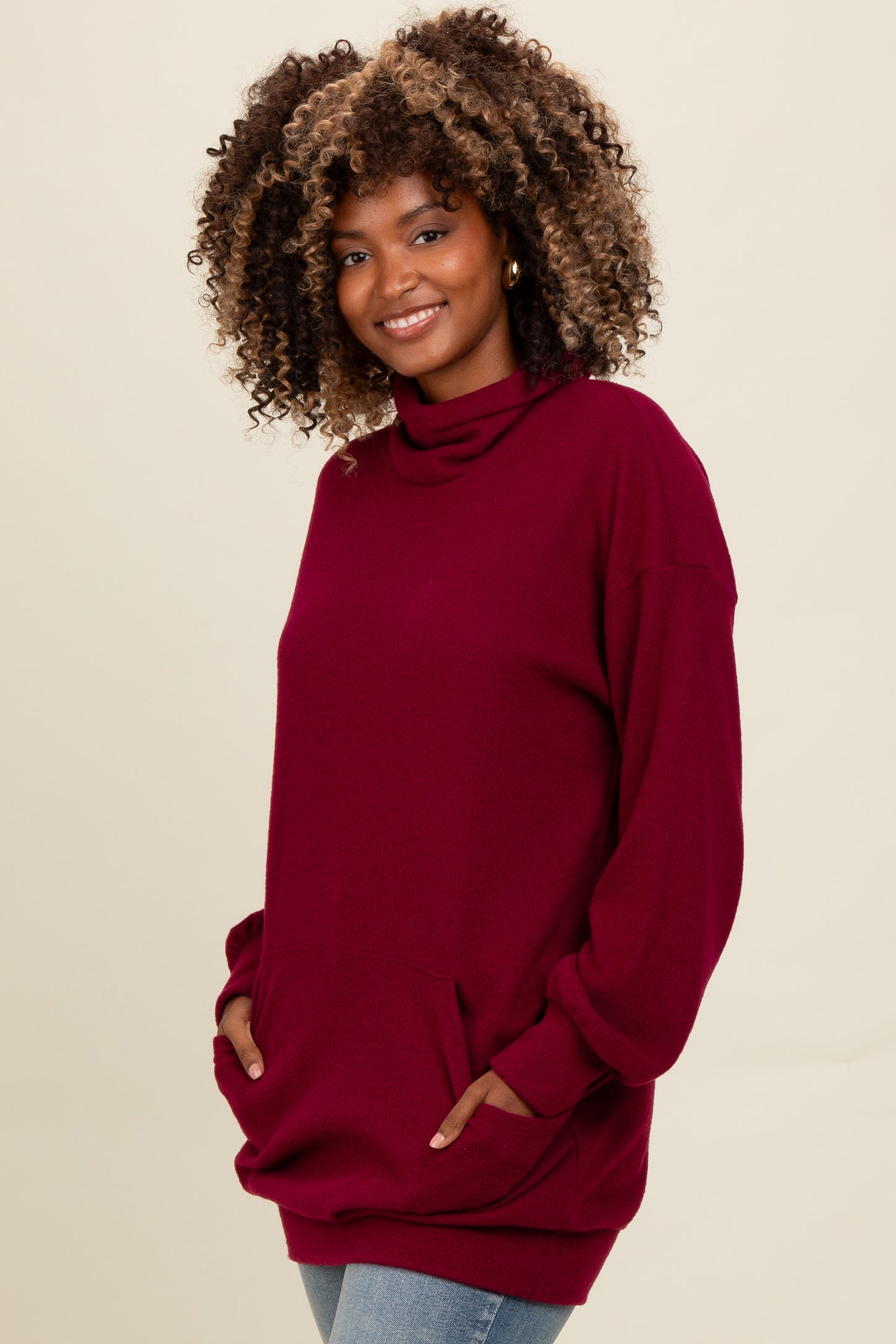 woman wearing a burgundy oversized cowl neck sweatshirt with pockets and long sleeves, styled with light blue jeans