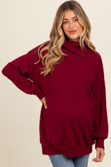 woman wearing a burgundy maternity sweatshirt with a cowl neck and front pocket, showing her baby bump