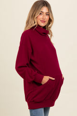 woman wearing a burgundy oversized turtleneck maternity sweatshirt with pockets and a visible baby bump