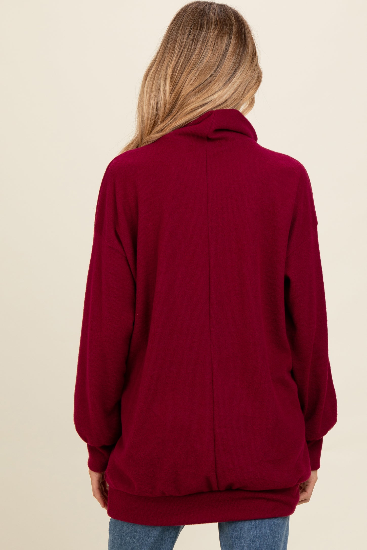woman wearing a burgundy maternity oversized sweater with a high neck and loose fit, viewed from the back