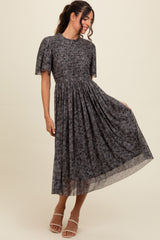 woman wearing a dark floral midi dress with puff sleeves and a cinched waist, posing with one hand on her hip
