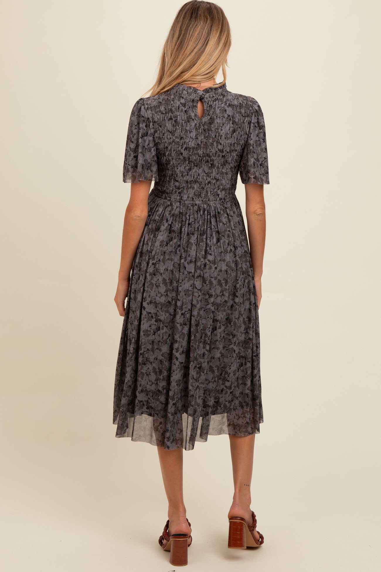 woman wearing a grey floral maternity dress with a smocked back and knee-length skirt, seen from the back