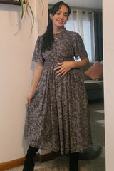 woman wearing a floral print maternity dress with a smocked bodice and short sleeves, gently cradling her baby bump