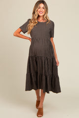 woman wearing a brown and black checked maternity dress with tiered skirts and short sleeves, showing her baby bump
