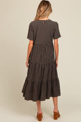 woman wearing a black and brown checkered maternity dress with tiered ruffles and short sleeves, with a button closure at the back