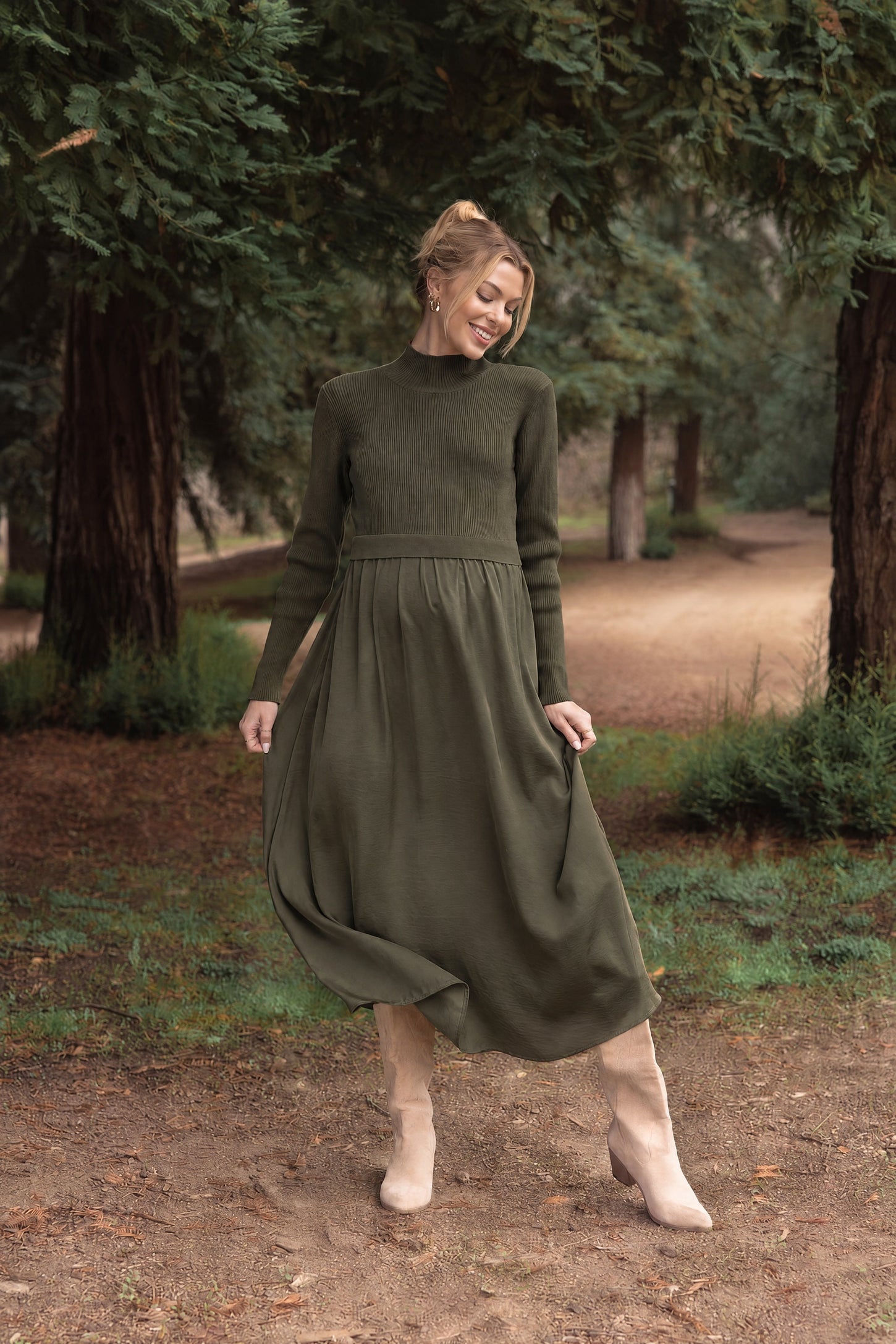 woman wearing an olive green maternity dress with long sleeves and a flowing skirt in a wooded outdoor setting