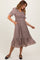 woman wearing a brown floral midi dress with puff sleeves and pockets, smiling while standing to the side