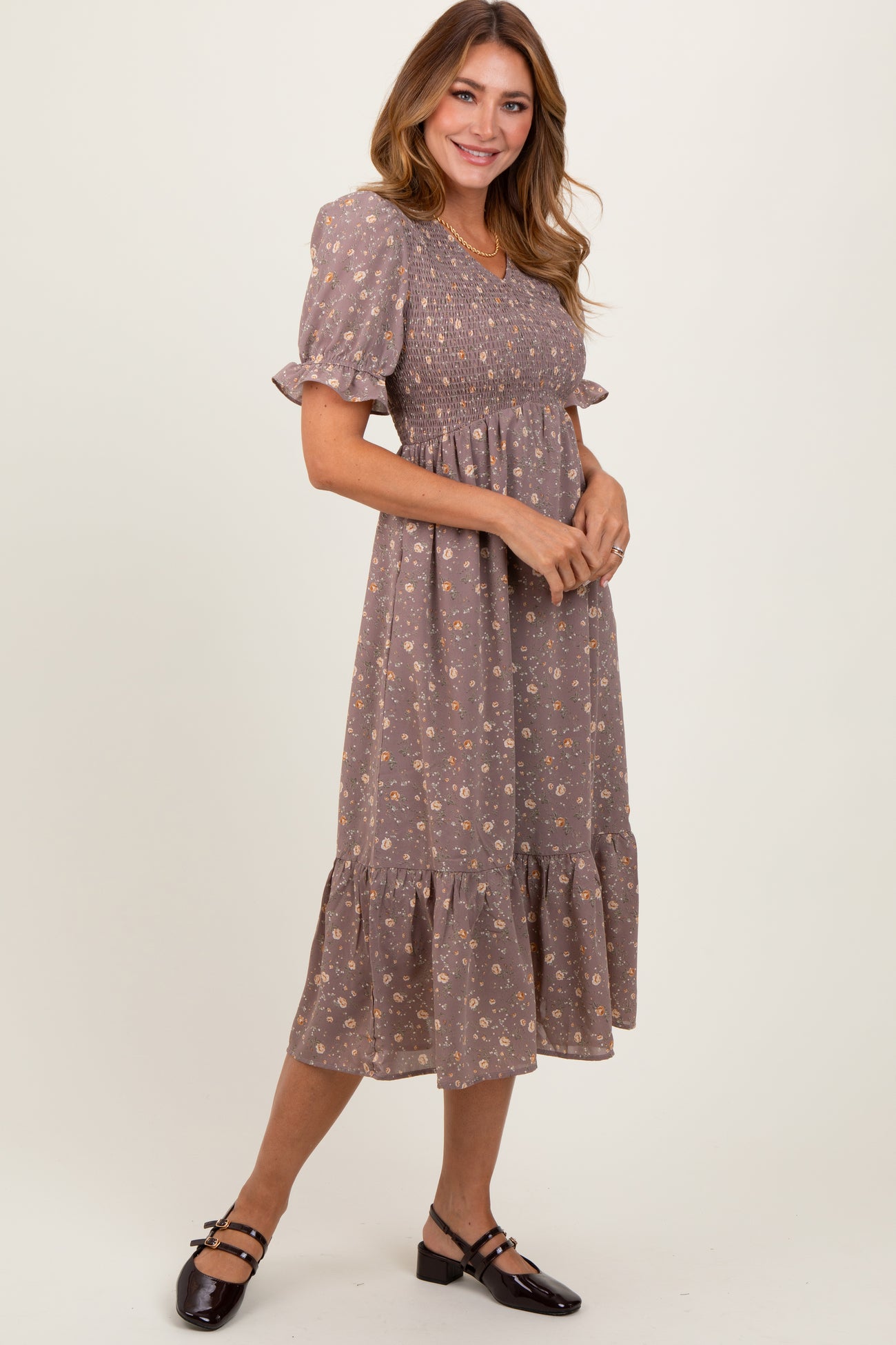 woman wearing a brown floral midi dress with puff sleeves and a ruffled hem, styled with black shoes