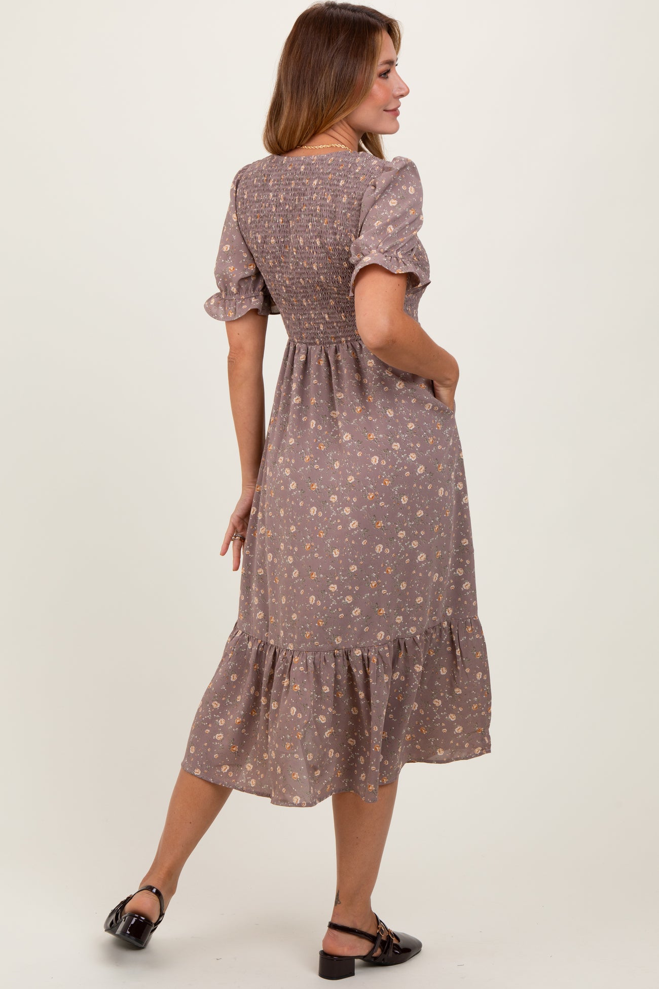woman wearing a dusty mauve floral short sleeve dress with a smocked back and tiered hem, standing with her back to the camera