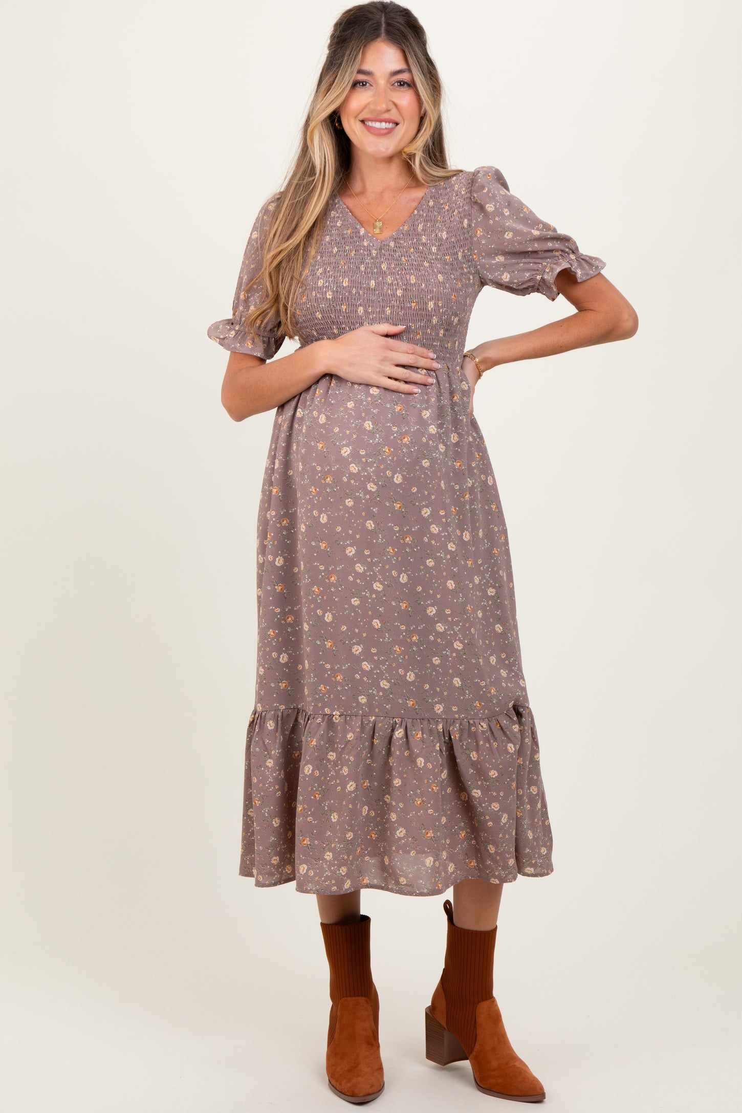woman wearing a brown floral maternity dress with puff sleeves and a ruffled hem, holding her baby bump