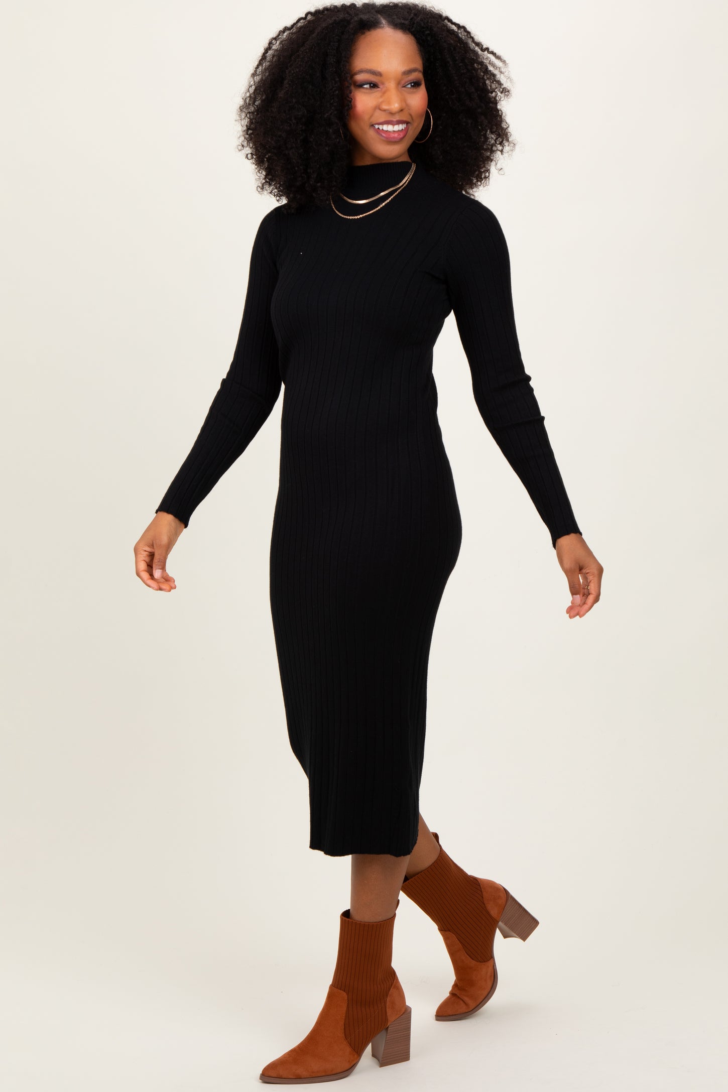 woman wearing a black ribbed turtleneck midi dress and tan ankle boots, smiling while walking