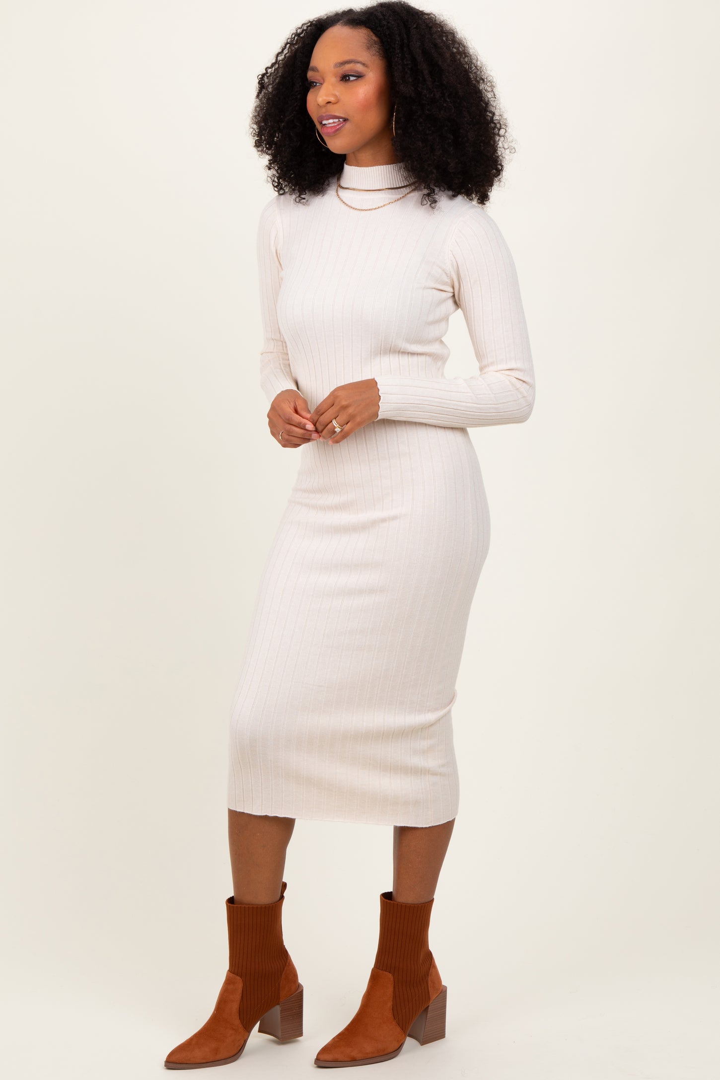 woman wearing a cream ribbed long sleeve midi dress with a mock neck and brown ankle boots