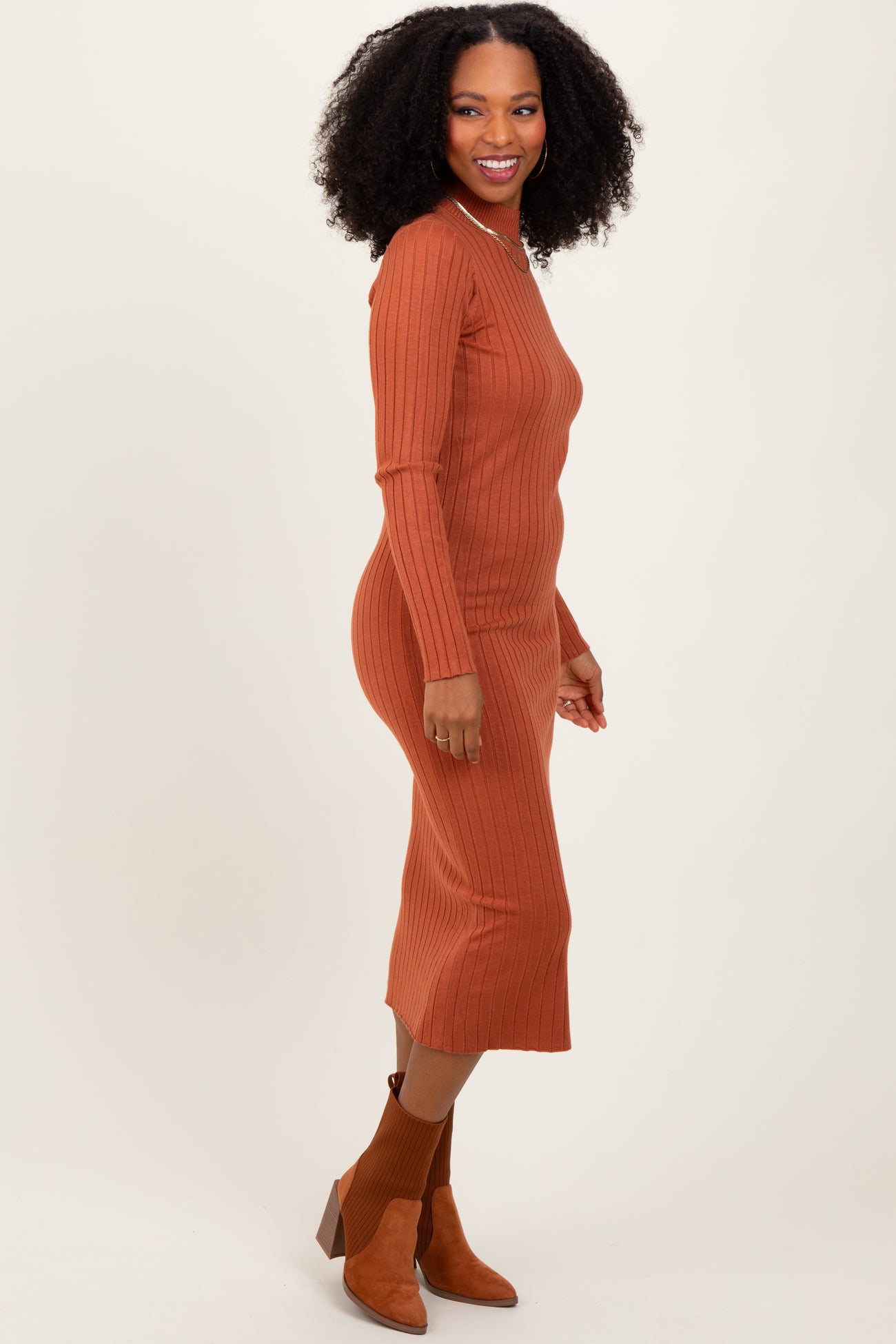 woman wearing a rust ribbed midi dress with long sleeves and a fitted silhouette, paired with brown heeled ankle boots