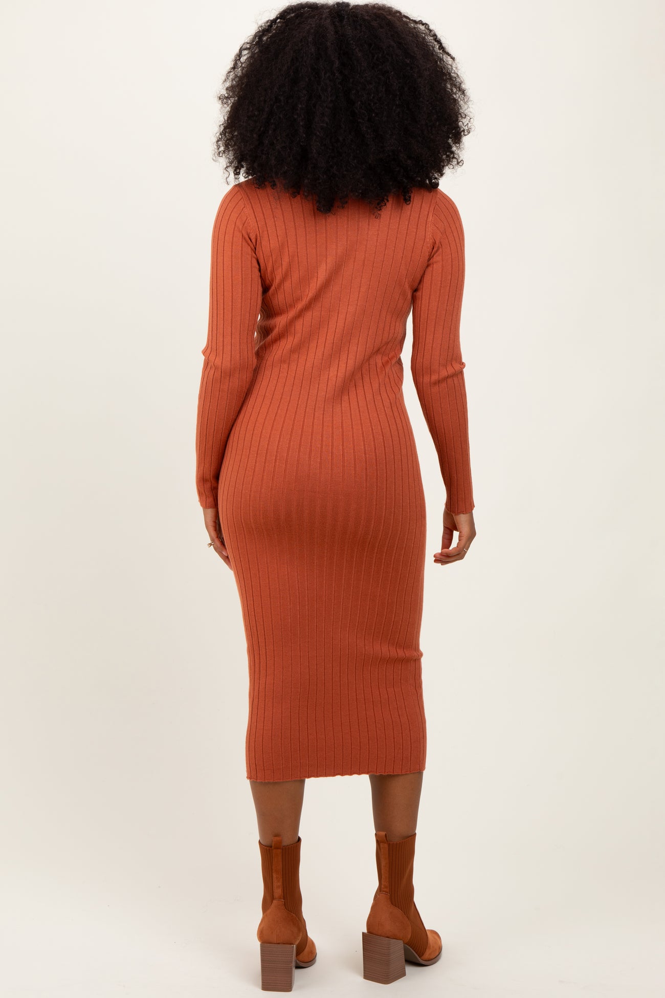 woman wearing a rust colored ribbed long sleeve midi dress and brown ankle boots, viewed from the back