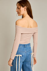 woman wearing a light pink off-the-shoulder long sleeve top paired with high-waisted blue jeans