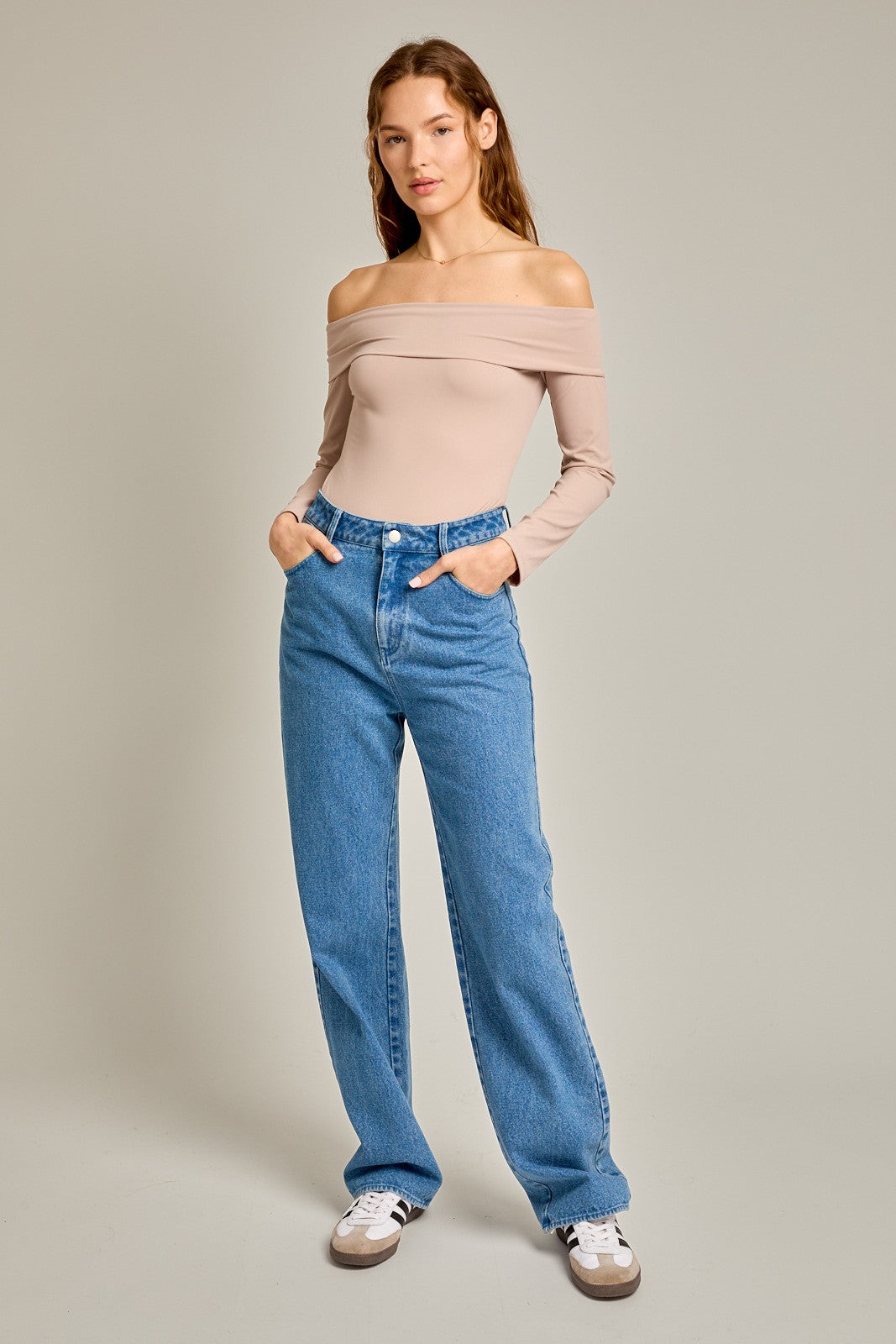 woman wearing a nude off-the-shoulder long sleeve bodysuit with high-waisted blue denim jeans and sneakers