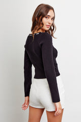 woman wearing a black fitted ribbed long sleeve top with back button detail and white sequined shorts