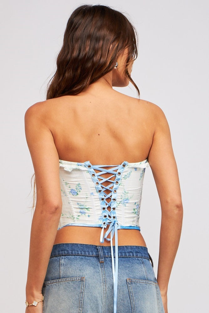 woman wearing a floral print strapless corset top with lace-up details, paired with denim shorts