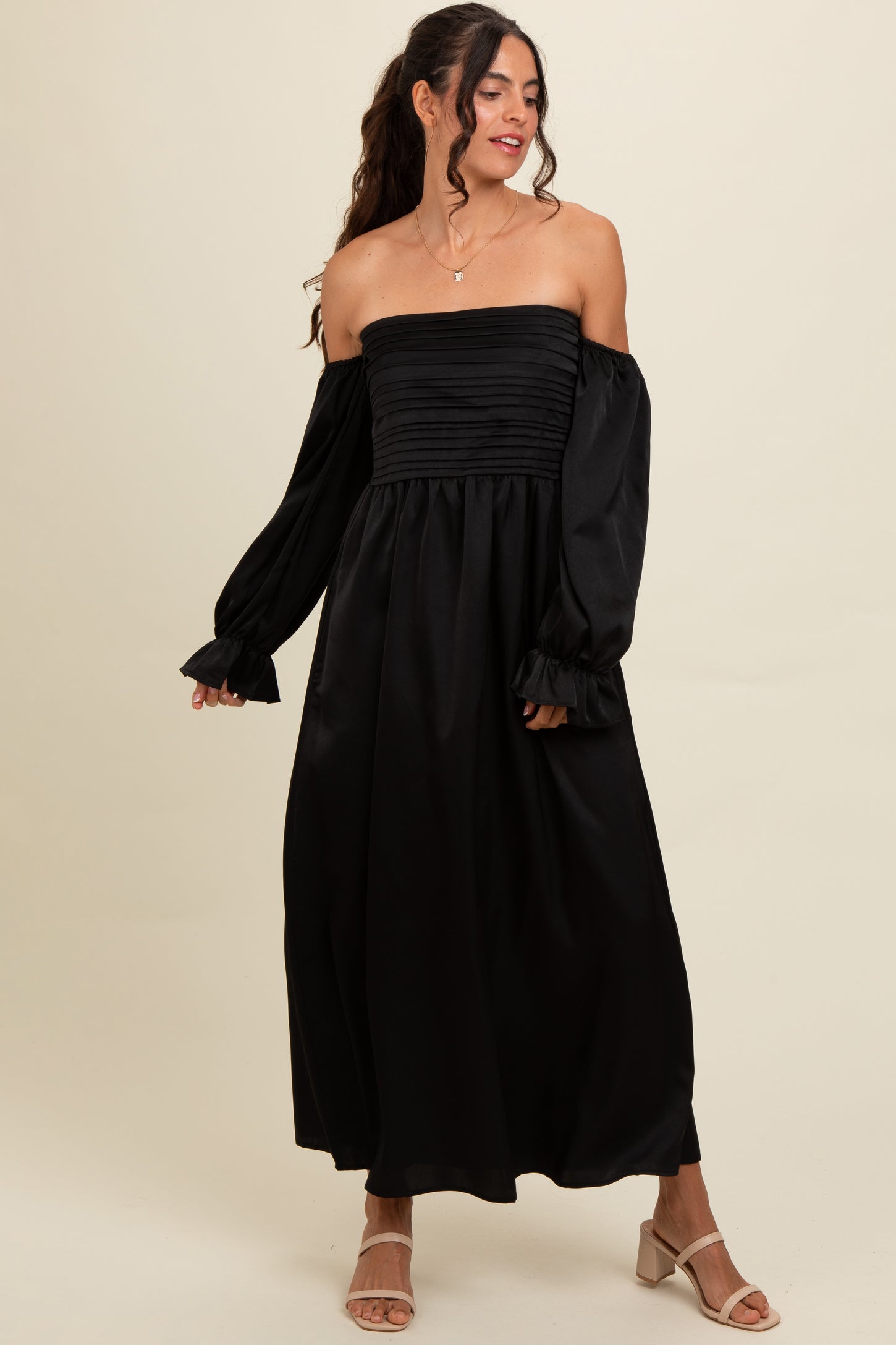 woman wearing a black off-the-shoulder maxi dress with ruched bodice and puff sleeves, styled with light-colored sandals