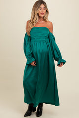 woman wearing a green off-the-shoulder maternity dress with long puff sleeves and a flowing maxi length, showcasing her baby bump