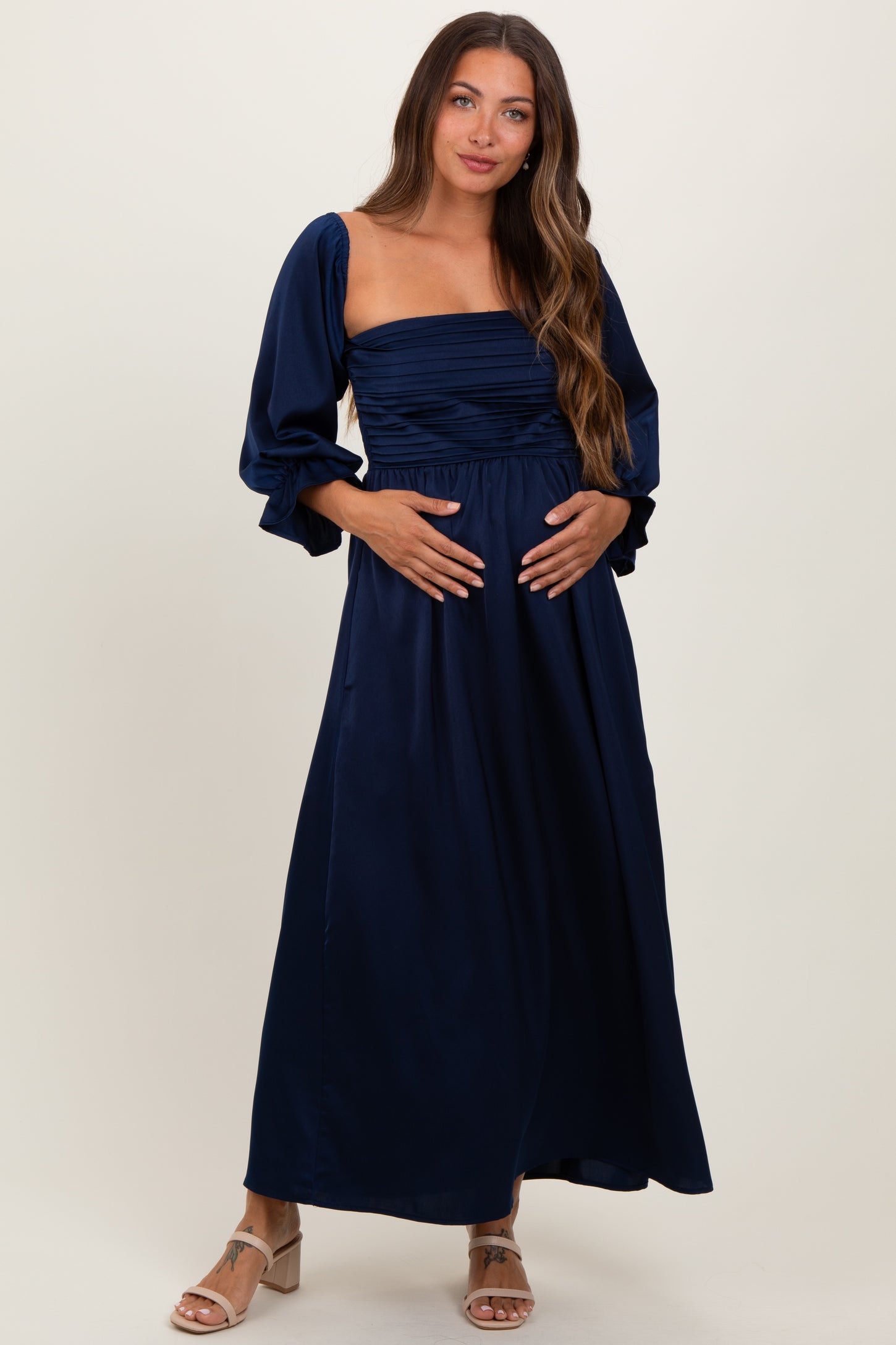 woman wearing a navy blue maternity maxi dress with puff sleeves and ruched bodice, showing her baby bump