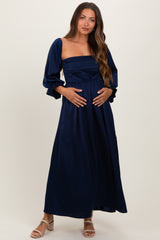 woman wearing a navy blue maternity maxi dress with puff sleeves and ruched bodice, showing her baby bump