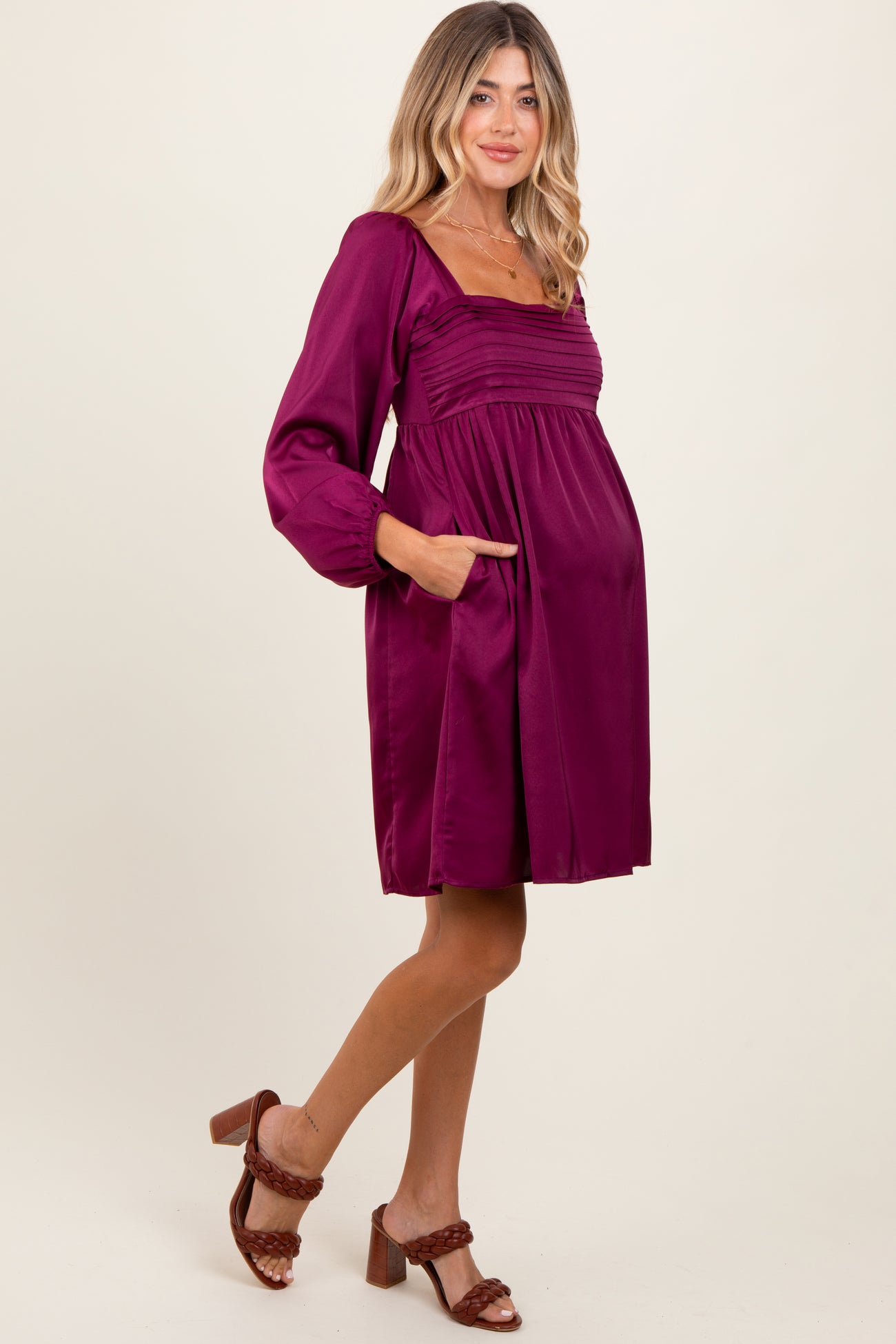 woman wearing a burgundy maternity dress with long sleeves and pockets, showing her baby bump