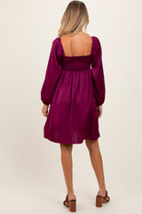 woman wearing a deep purple maternity dress with puffed sleeves and a smocked bodice, showing a relaxed fit