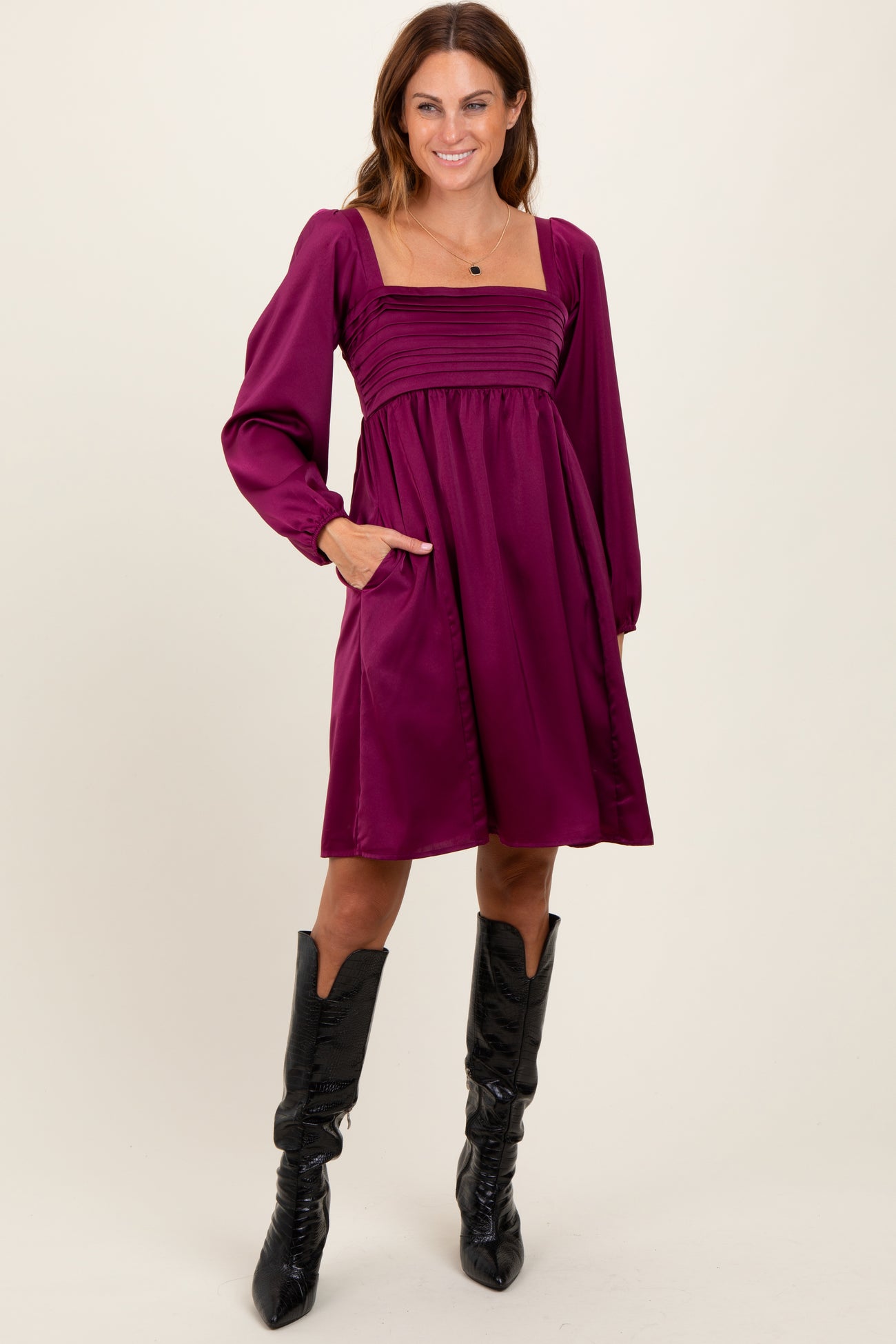 woman wearing a purple square neck dress with long puff sleeves and side pockets, styled with black knee-high boots
