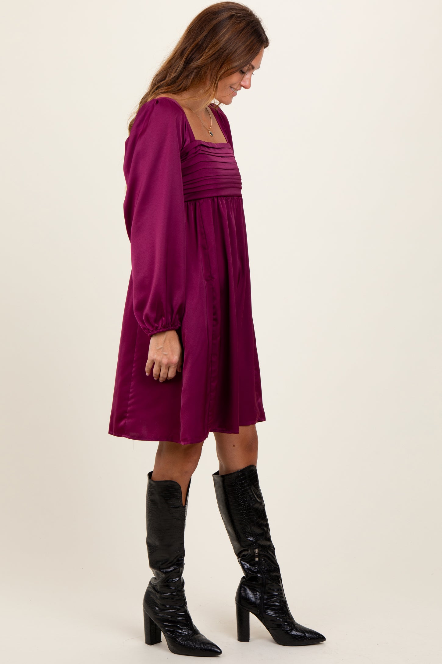 woman wearing a burgundy long sleeve dress with pleated detail and black knee-high boots