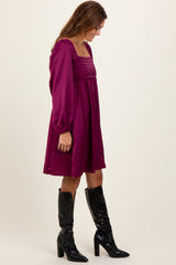 woman wearing a burgundy long sleeve dress with pleated detail and black knee-high boots