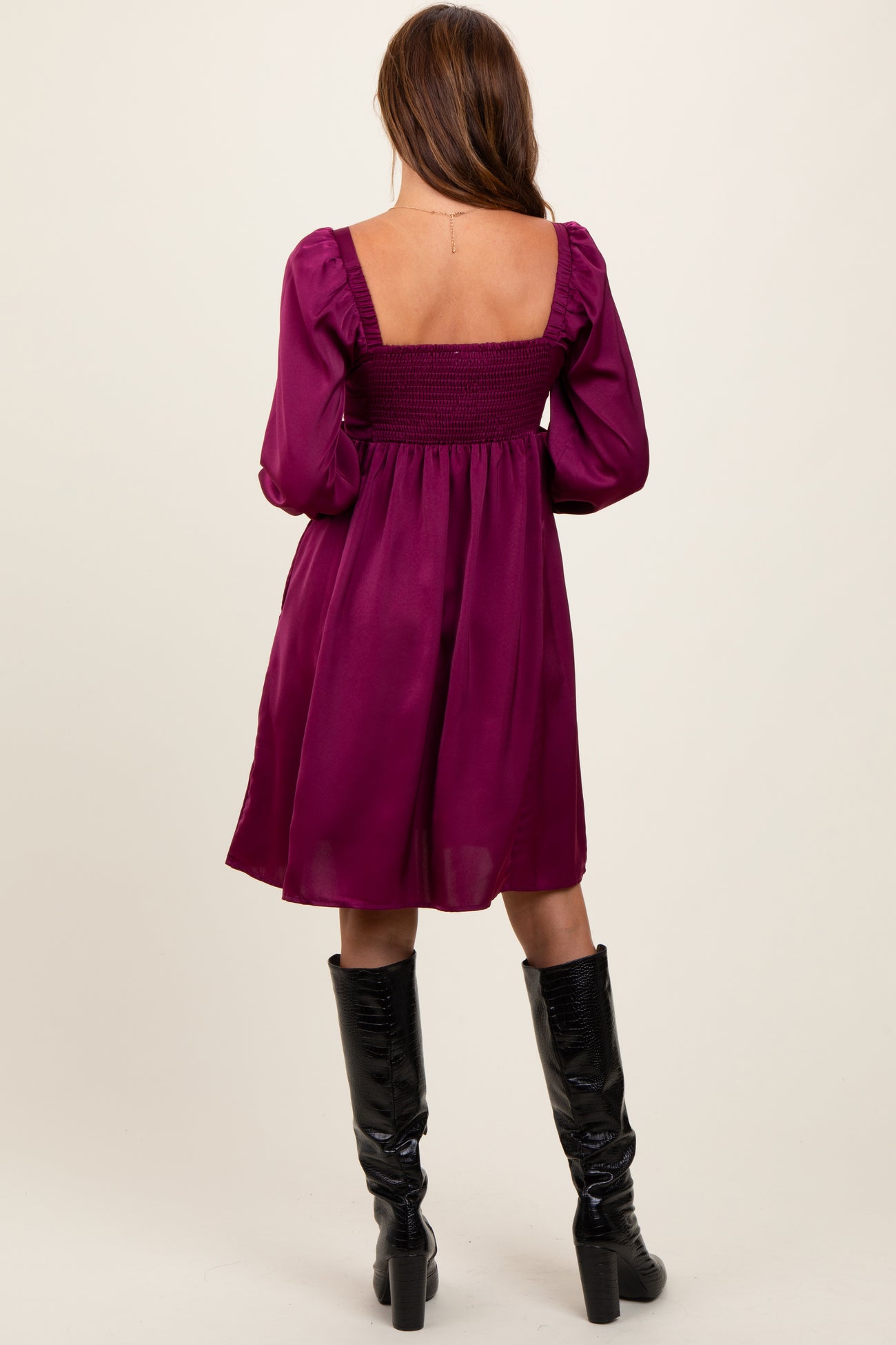 woman wearing a plum purple smocked back dress with puff sleeves and knee-high black boots