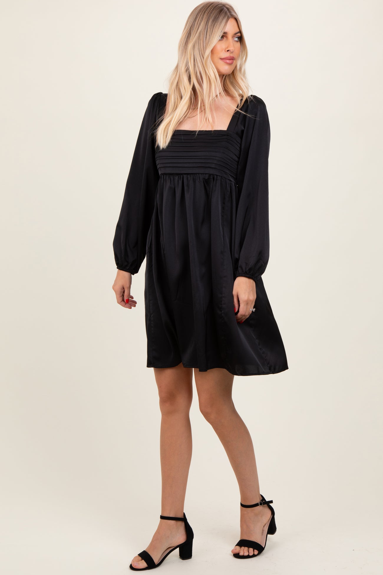 woman wearing a black short dress with puff sleeves and a square neckline, styled with black heels